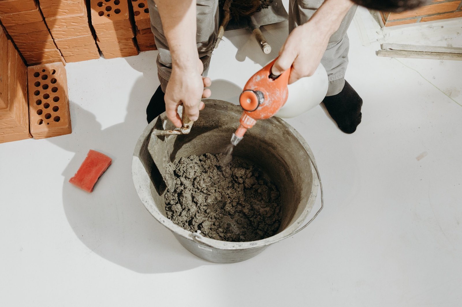 Construction worker adding water while mixing cement-based mortar in a bucket