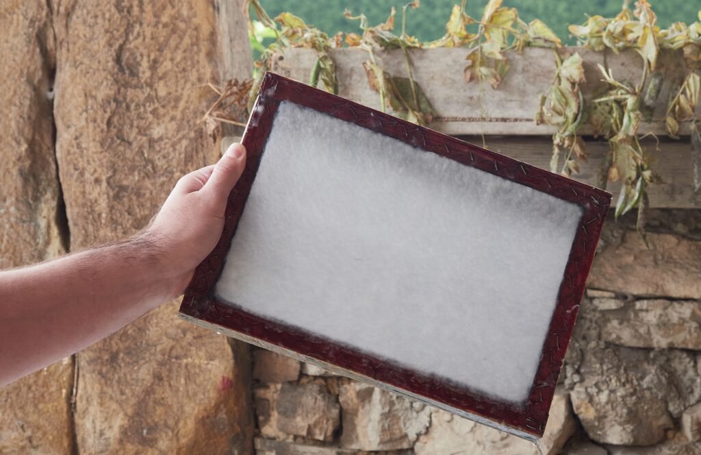 Craftsman's hands holding a wooden frame with vegetable fibers to make sheets of paper.