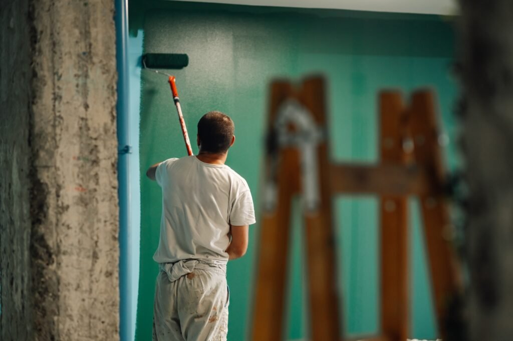 Painter painting wall with paint roller in turquoise room