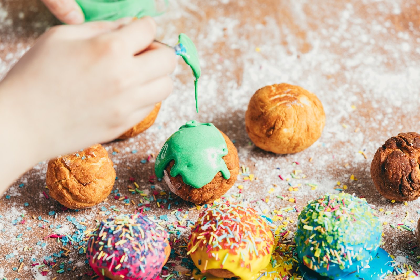 Woman's hand coating a donut with green frosting.