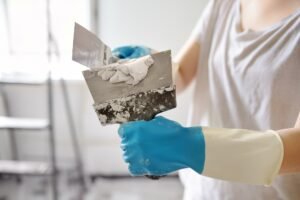 Young female worker preparing putty for wall repair. Close-up view of spreading plaster on spatula