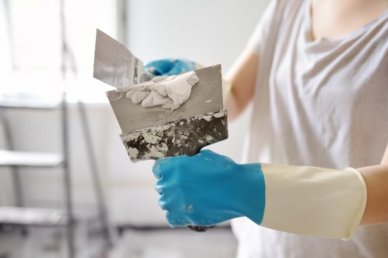 Young female worker preparing putty for wall repair. Close-up view of spreading plaster on spatula